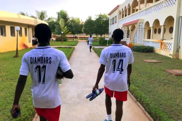 Deux joueurs en tenue blanche et short rouge marchent vers le terrain